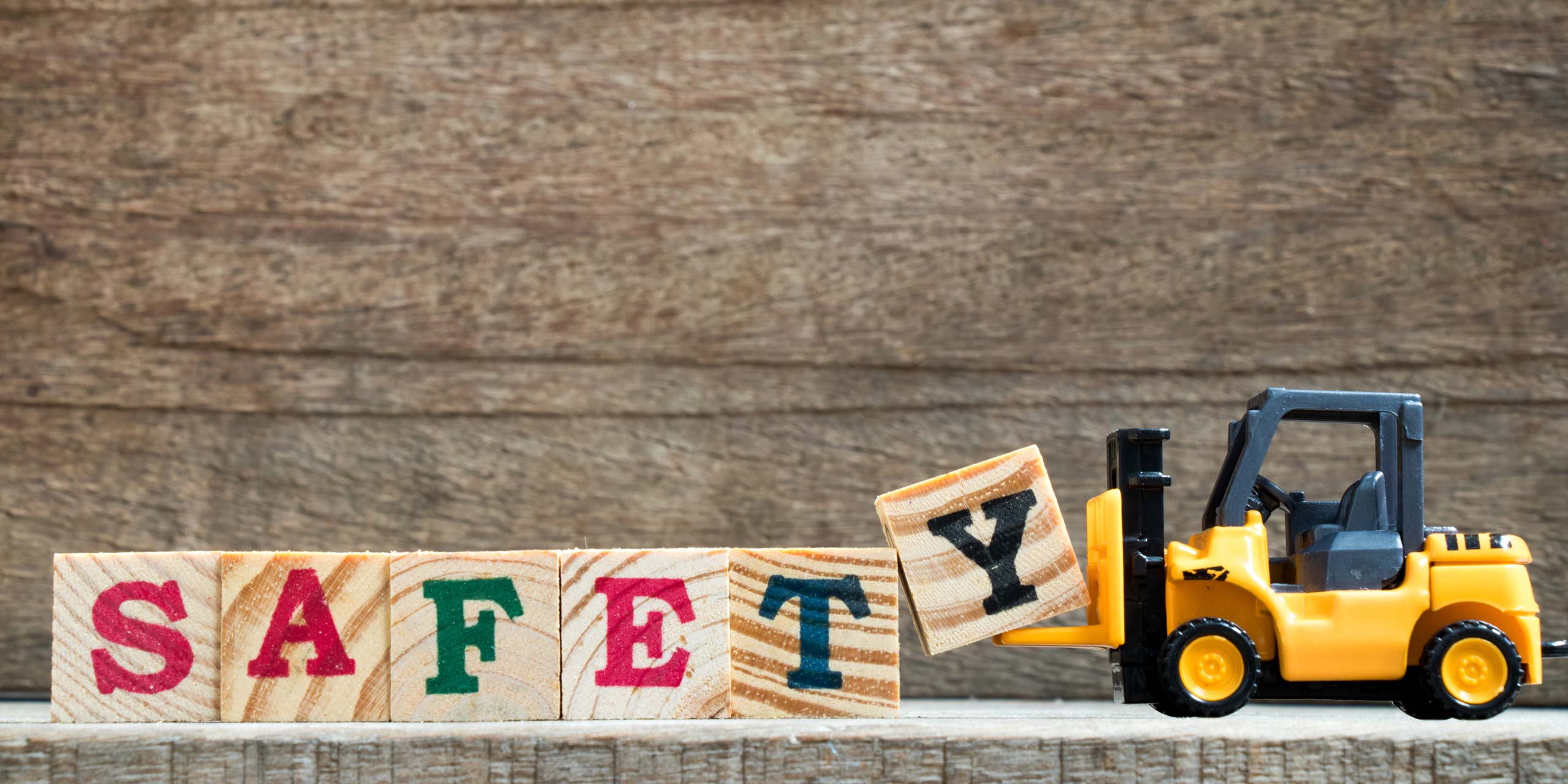 Spielzeuggabelstapler der das englische Wort Safefy, also Sicherheit, mit bedruckten Holzwürfeln zusammenstellt.